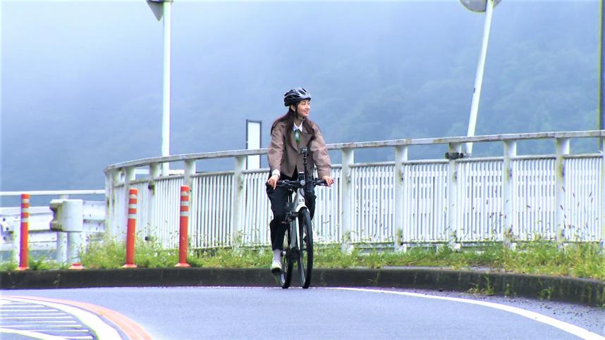 テレビ写真(e-bikeに乗り、やまびこ大橋を横断する熊井リポーター)