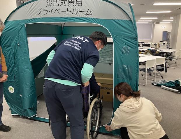 避難所内テントに車いすに乗る被災者の方を誘導している写真