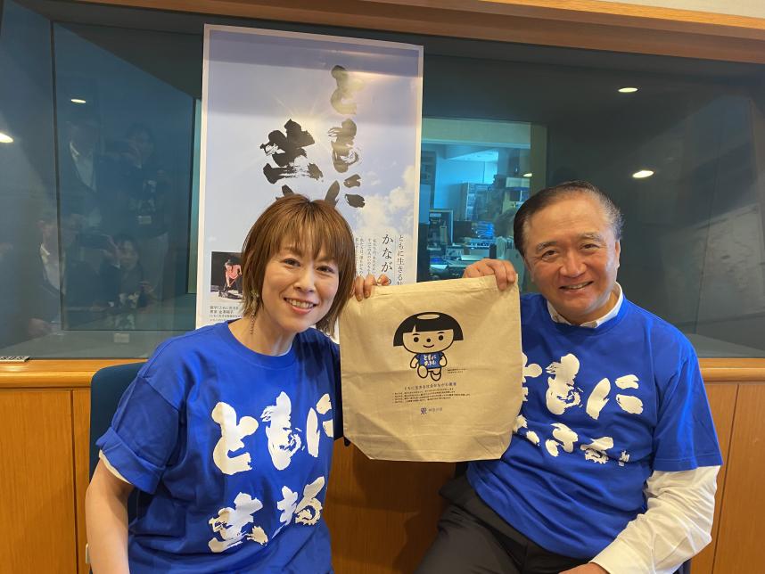 ラジオ写真（リスナープレゼントのコットンバックを挟んで、ともいきTシャツ着用の左から金子パーソナリティと黒岩知事）