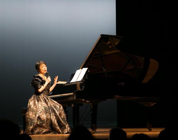 写真：ピアノの横でお話しする熊本マリさん