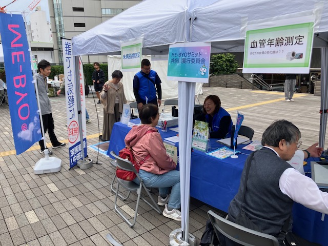 屋外イベント会場のME-BYOブースで、来場者が測定案内を受けている様子