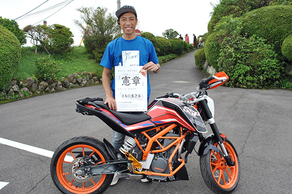 青木治親さん。SSPで作った補助輪付きバイクとともに