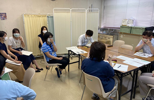 部屋の中で会議している風景写真（人は皆、マスクをつけている）。