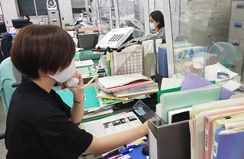 オフィス内で電話をとっている風景写真（人は皆、マスクをつけている）。